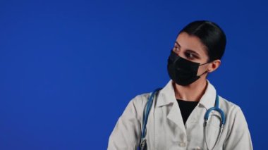 Mavi arka planda siyah bir tıbbi maske takan kadın sağlık çalışanı. Bir doktorun portresi. Viroloji ve salgın konsepti