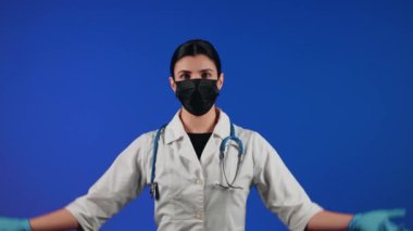 Mavi arka planda siyah bir tıbbi maske takan kadın sağlık çalışanı. Bir doktorun portresi. Viroloji ve salgın konsepti