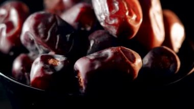 Dried dates rotate on a black background showcasing their rich texture in a close-up view