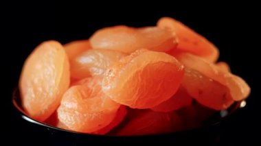 Siyah bir arkaplan üzerinde dönen kuruyan kayısıların canlı dokusunu ve zengin rengini keşfedin