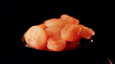 Siyah bir arkaplan üzerinde dönen kuruyan kayısıların canlı dokusunu ve zengin rengini keşfedin