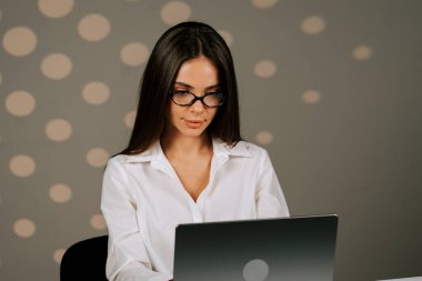 Successful business woman working at a laptop in a modern office environment with soft lighting in the background clipart