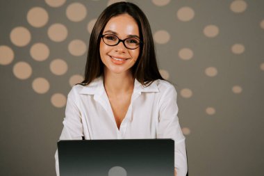 Successful business woman working at a laptop in a modern office environment with soft lighting in the background clipart