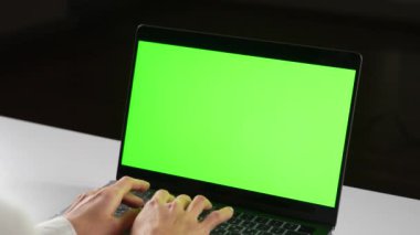 Parlak yeşil ekranlı bir dizüstü bilgisayarla loş ışıklı bir odada görevlerine odaklanmış bir kadın.