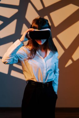 Sanal gerçeklik gözlüğü takmış, dijital dünyayı keşfeden bir kadın ilginç bir deneyimde renkli bir arka plana karşı çıkıyor.