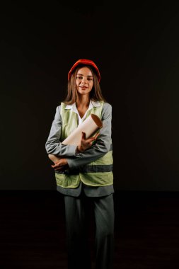 Woman engineer wearing safety gear and helmet, smiling confidently on a black background clipart