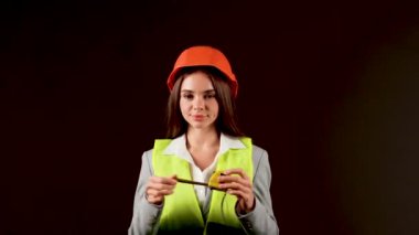 Stüdyoda güvenlik donanımı takan kadın mühendis, siyah arka planda işini güçlendirici bir anda yapıyor.