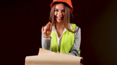 Stüdyoda güvenlik donanımı takan kadın mühendis, siyah arka planda işini güçlendirici bir anda yapıyor.