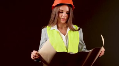 Stüdyoda güvenlik donanımı takan kadın mühendis, siyah arka planda işini güçlendirici bir anda yapıyor.