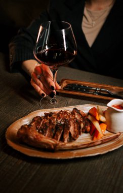 Delicious meat dish with sauce served on a wooden plate paired with a glass of red wine in a cozy dining setting clipart