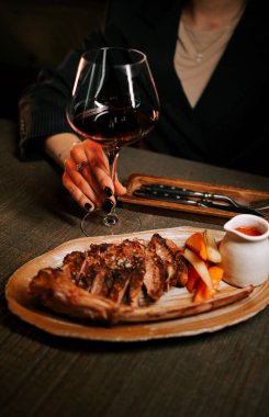 Delicious meat dish with sauce served on a wooden plate paired with a glass of red wine in a cozy dining setting clipart