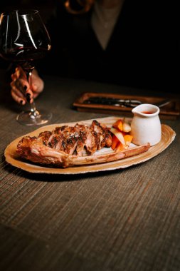 Delicious meat dish with sauce served on a wooden plate paired with a glass of red wine in a cozy dining setting clipart