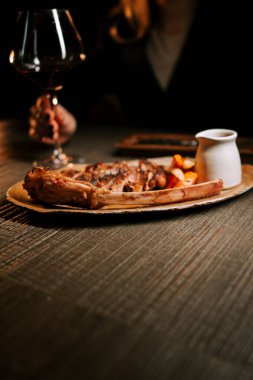 Ahşap bir tabakta servis edilen soslu leziz et tabağı ve sıcak bir yemek ortamında bir bardak kırmızı şarap.