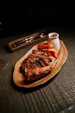 Ahşap bir tabakta servis edilen soslu leziz et tabağı ve sıcak bir yemek ortamında bir bardak kırmızı şarap.