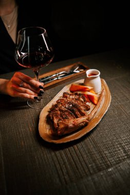 Ahşap bir tabakta servis edilen soslu leziz et tabağı ve sıcak bir yemek ortamında bir bardak kırmızı şarap.