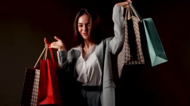 Alışveriş merkezinde şık giysiler içinde alışveriş yapan bir kadın elinde bir sürü renkli çanta tutuyor.