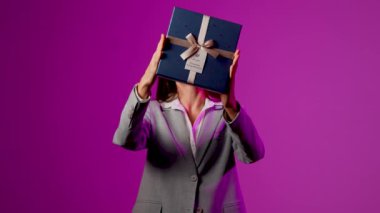 Heyecanlı kadın canlı bir sunum sırasında canlı mor arka plana karşı sürpriz bir hediye açıyor.