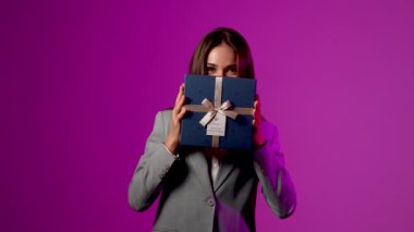 Heyecanlı kadın canlı bir sunum sırasında canlı mor arka plana karşı sürpriz bir hediye açıyor.