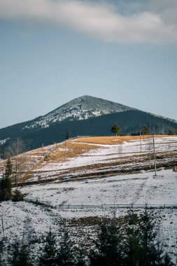 Kış mevsiminde ahşap aksanlı modern mimarinin yer aldığı dağ manzarası, karla kaplı arazi ve ormanları gözler önüne seriyor