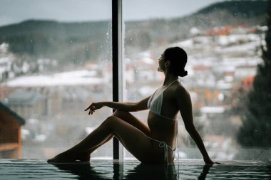 Bulutlu bir günde dağ manzaralı sakin bir havuzda dinlenen bir kadın.