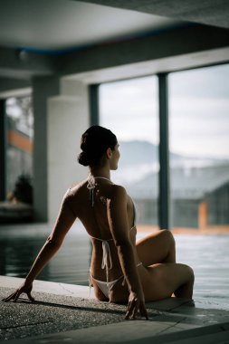 Gündüz vakti sakin bir dağ ortamında lüks bir kapalı havuzda dinlenen bir kadın.