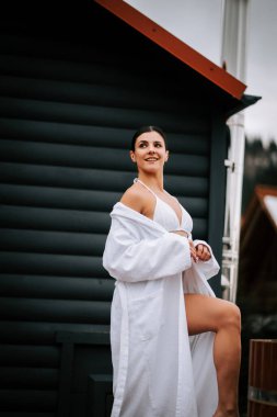 Beyaz mayo giymiş bir kadın, kışın dağlarla çevrili sıcak su fıçısına giriyor..