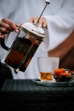 Beyaz cüppeli kadın, sakin bir sabah boyunca terasta karla kaplı dağlarla çay içmeyi sever.