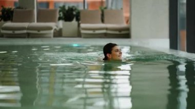 Beyaz mayo giyen kadın kış tatili kaçamağı sırasında karlı dağ manzaralı spa havuzunun keyfini çıkarıyor.