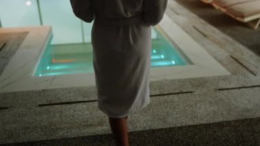 Beyaz mayo giyen kadın kış tatili kaçamağı sırasında karlı dağ manzaralı spa havuzunun keyfini çıkarıyor.