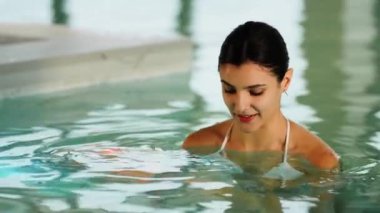 Beyaz mayo giyen kadın kış tatili kaçamağı sırasında karlı dağ manzaralı spa havuzunun keyfini çıkarıyor.
