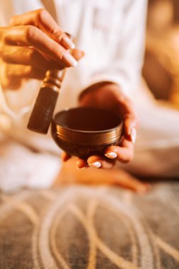 Yumuşak ışıkla aydınlatılmış, dingin bir odada Tibet şarkı kasesiyle meditasyon yapan bir kadın.