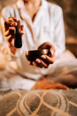 Yumuşak ışıkla aydınlatılmış, dingin bir odada Tibet şarkı kasesiyle meditasyon yapan bir kadın.