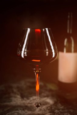 Koyu yüzeyde, kırmızı şarap kadehinin yanında ince yansımalar ve sıcak ışık efektleri var.