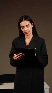 Bir ofis ortamında dizüstü bilgisayar ve pano kullanarak belgeleri inceleyen profesyonel bir kadın.