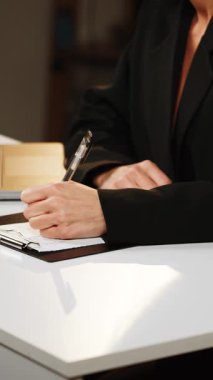 Bir ofis ortamında dizüstü bilgisayar ve pano kullanarak belgeleri inceleyen profesyonel bir kadın.