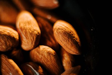 Taze kavrulmuş bademler, siyah bir kâsede altın-kahverengi rengini vurgulayan koyu bir arka plana karşı servis edilir.