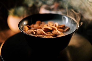 Freshly roasted almonds served in a black bowl against a dark background highlighting their golden-brown color clipart