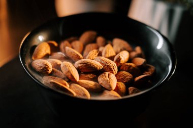 Freshly roasted almonds served in a black bowl against a dark background highlighting their golden-brown color clipart