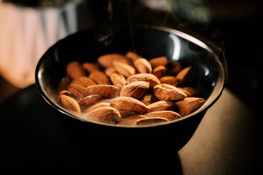 Taze kavrulmuş bademler, siyah bir kâsede altın-kahverengi rengini vurgulayan koyu bir arka plana karşı servis edilir.