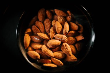 Taze kavrulmuş bademler, siyah bir kâsede altın-kahverengi rengini vurgulayan koyu bir arka plana karşı servis edilir.