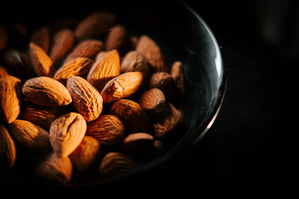 Freshly roasted almonds served in a black bowl against a dark background highlighting their golden-brown color