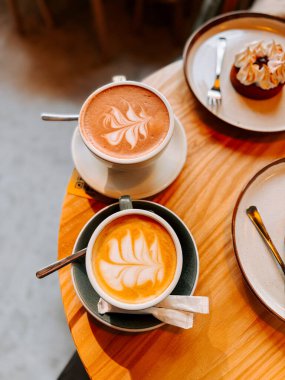 Sabah saatlerinde rahat bir kafede, ahşap bir masada servis edilen iki fincan latte.