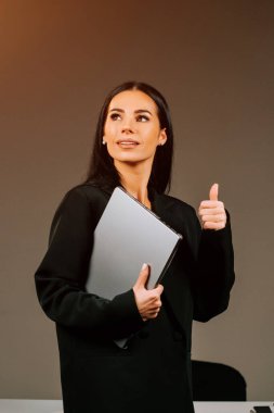 Modern ofis ortamında kendine güvenen bir gülümsemeyle dizüstü bilgisayarda çalışan profesyonel bir kadın.