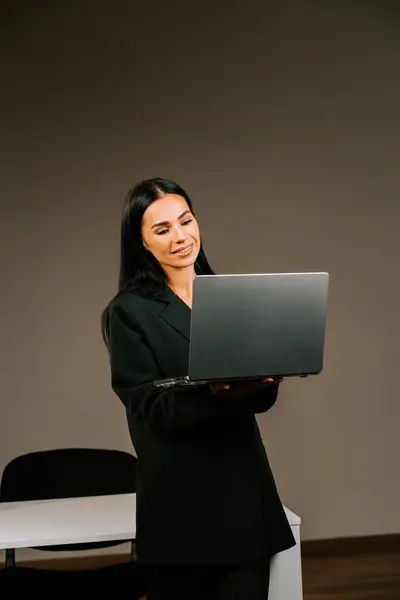 Modern ofis ortamında kendine güvenen bir gülümsemeyle dizüstü bilgisayarda çalışan profesyonel bir kadın.