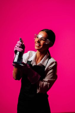 Kendine güvenen bir temizlikçinin portresi canlı pembe bir arka plana karşı eldiven takıyor. Temizliğe olan bağlılığını gösteriyor.