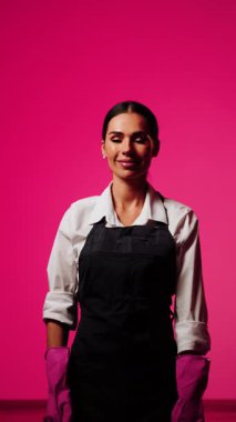 Canlı pembe arka planda aletlerle temizlik yapan kadın ev temizleme konsepti ve profesyonelliği gösteriyor.