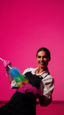 Canlı pembe arka planda aletlerle temizlik yapan kadın ev temizleme konsepti ve profesyonelliği gösteriyor.