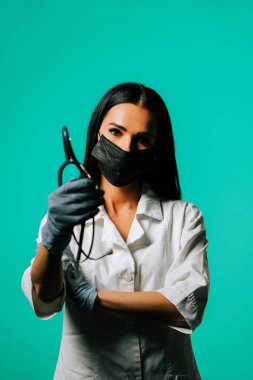 Genç sağlık uzmanı, klinik ortamda canlı bir turkuaz arka plana güvenle gülümsüyor.