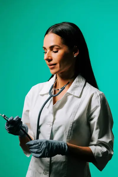 Genç sağlık uzmanı, klinik ortamda canlı bir turkuaz arka plana güvenle gülümsüyor.