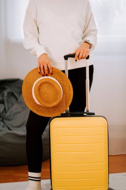 Sarı bavul ve hasır şapka modern bir ev ortamında heyecan verici bir tatil gezisine hazır.